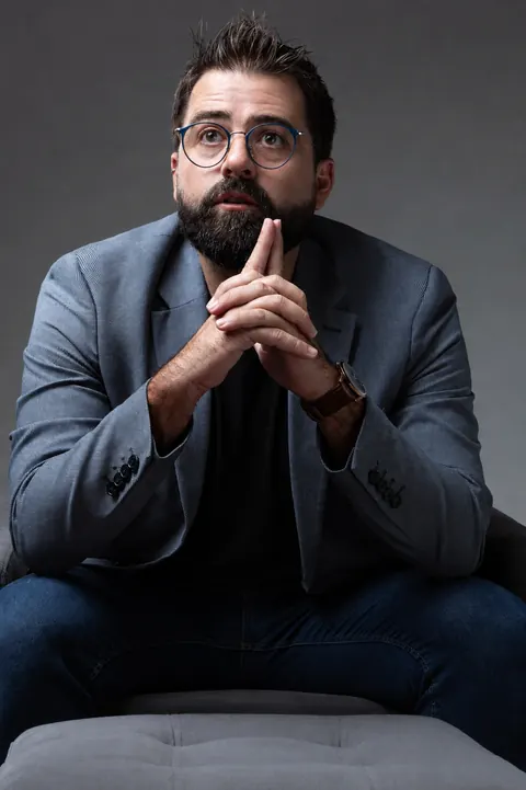 Romero de Deus sentado, mãos unidas próximas ao rosto, em postura de reflexão